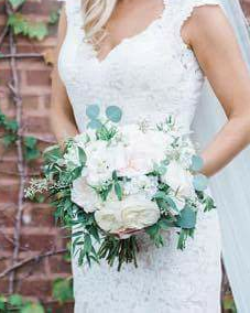 Bride holding a bouquet of white and green flowers in front of a brick wall