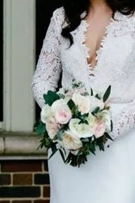 A woman in a white lace wedding dress holding a bouquet of white and pink flowers.