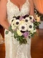 Bride holding a bouquet of white and purple flowers in a wedding dress.