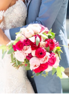 Bride and groom holding a colorful wedding bouquet with pink, white, and red flowers.
