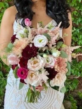 Person holding a large bouquet of pink, white, and burgundy flowers outside.
