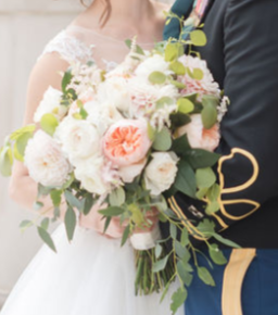 Close-up of a bride and groom holding a large bouquet of white, pink, and green flowers at their wedding.