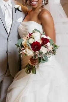 Bride holding a bouquet of white, red, and pink flowers at a wedding.