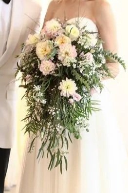 A person in a white dress holding a large bouquet of mixed flowers with greenery.