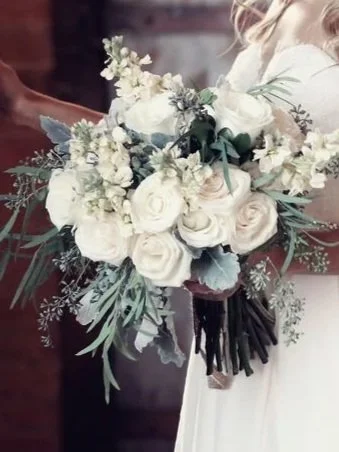 A bride holding a bouquet of white roses, peonies, and greenery.