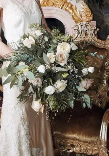 Close-up of a bride holding a large bouquet of white flowers and greenery during a wedding.