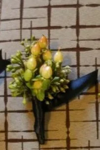 Close-up of a small bouquet of white and yellow flowers with green leaves, secured with black floral tape on a wooden surface.