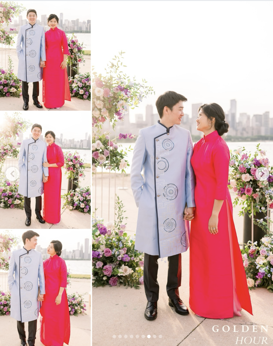 A couple dressed in traditional Vietnamese clothing, standing outdoors near water and city skyline, with floral decorations around them, during a daytime celebration.