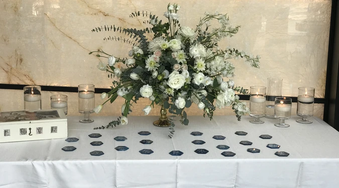 A table with a large floral arrangement, lit candles, and physical tokens or cards