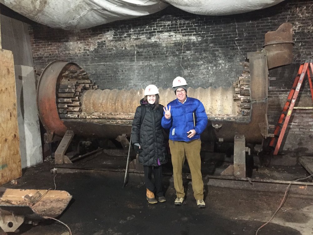   John McConnell, Founder and President, and Tara Hank, Development Office Coordinator, stand in front of the old boiler.&nbsp;  