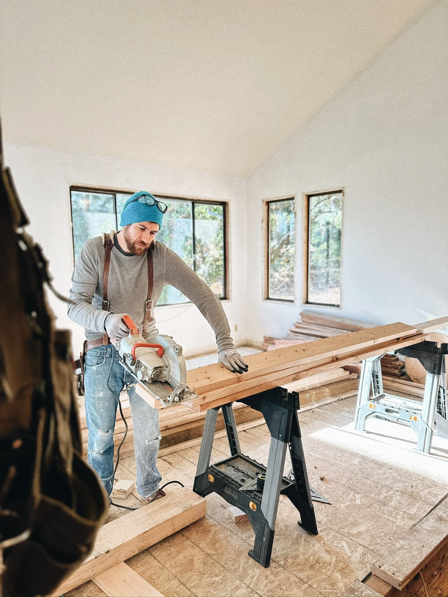 Carpenter wearing blue beanie using a circular saw on wood plank indoors