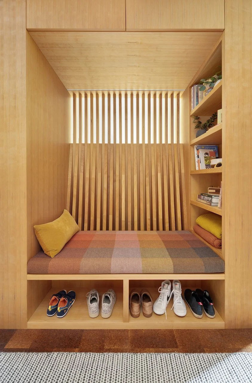 Cozy wooden alcove with a checkered cushion, pillow, bookshelf, and shoe storage.