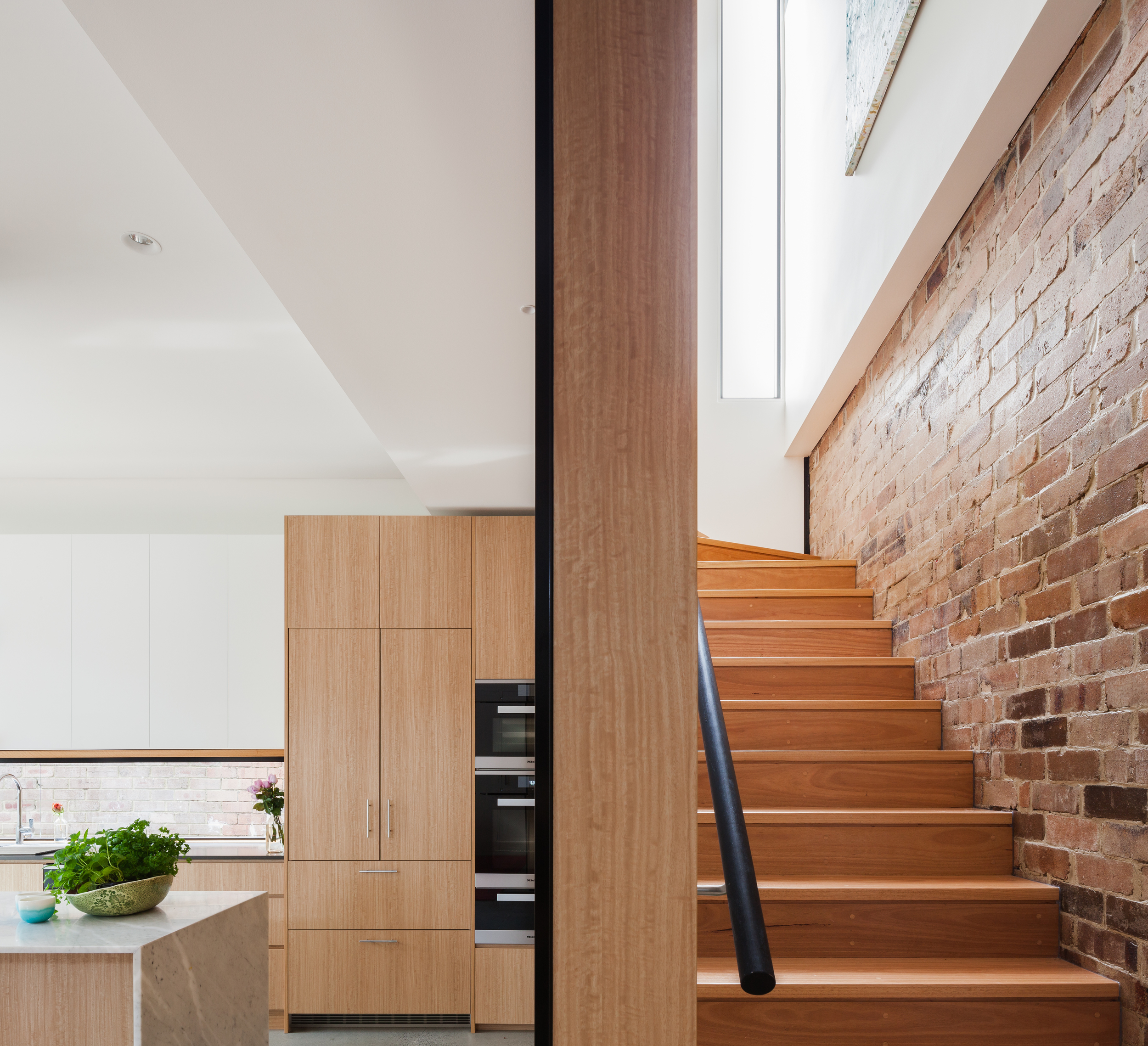 The existing brick wall of the old house is exposed to the new timber lined stair.