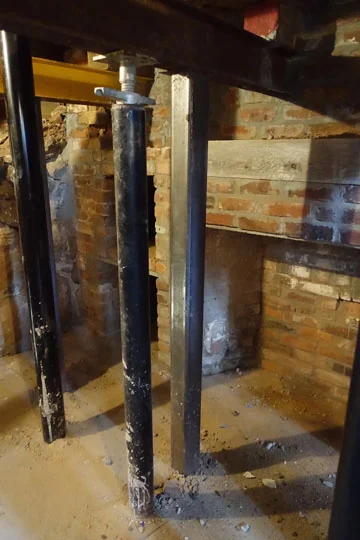 A temporary steel jack holds up a new steel beam as permanent posts are installed; at the front of the house the rubble stone cellar wall was collapsing and had to be reinforced and new brickwork at the chimneys repaired to make the house structurally sound.