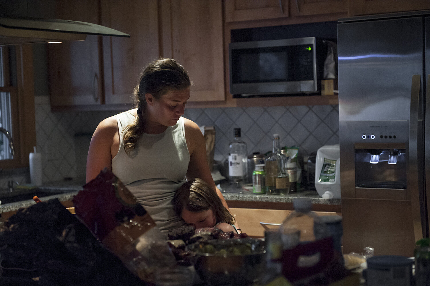 Bethany comforts her daughter, Cole, in the kitchen of her cousin’s camp, after a long day, and a cookout with family and friends. Cole is tired and upset that they haven’t gone for the long promised boat ride yet.