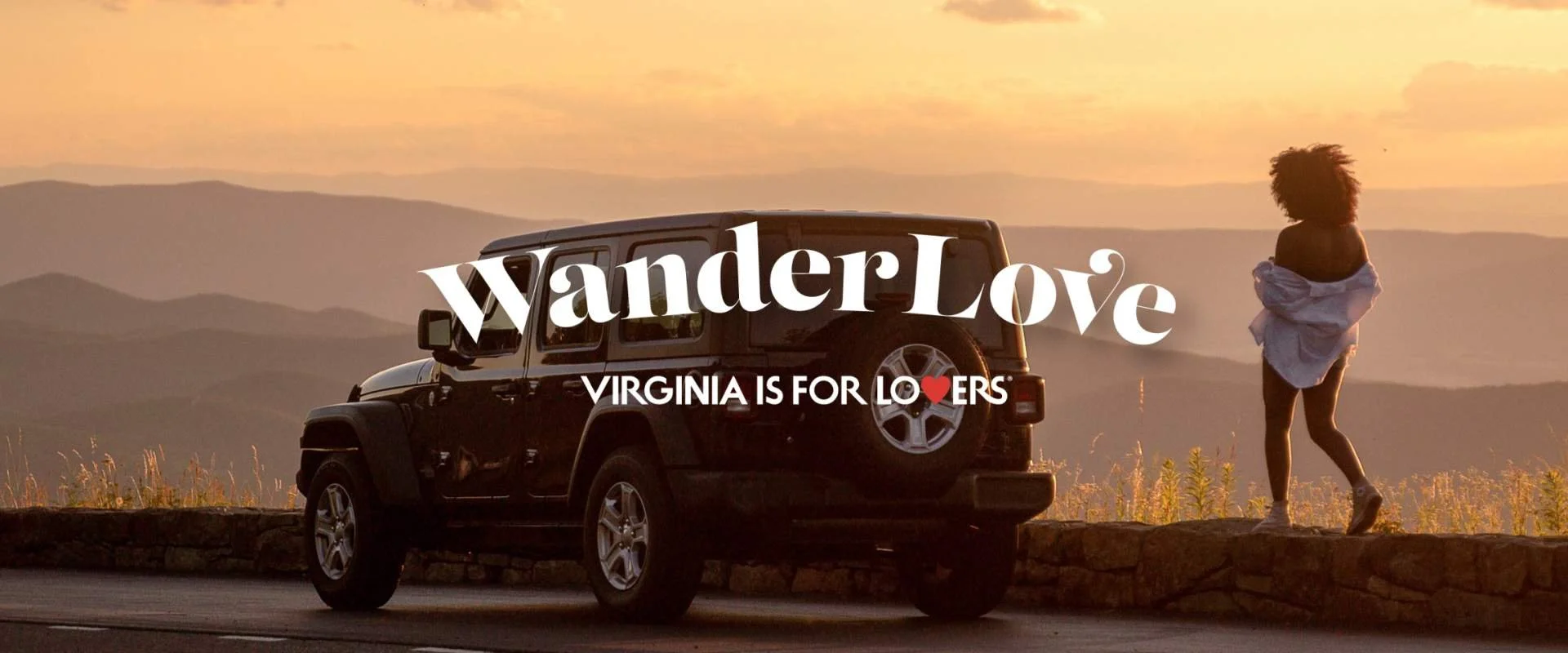 A woman with curly hair stands on a stone ledge, facing away, next to a black Jeep parked on the road, with a sunset and mountain range in the background. Overlaid text reads "WanderLove" and "Virginia is for Lovers" with a red heart.