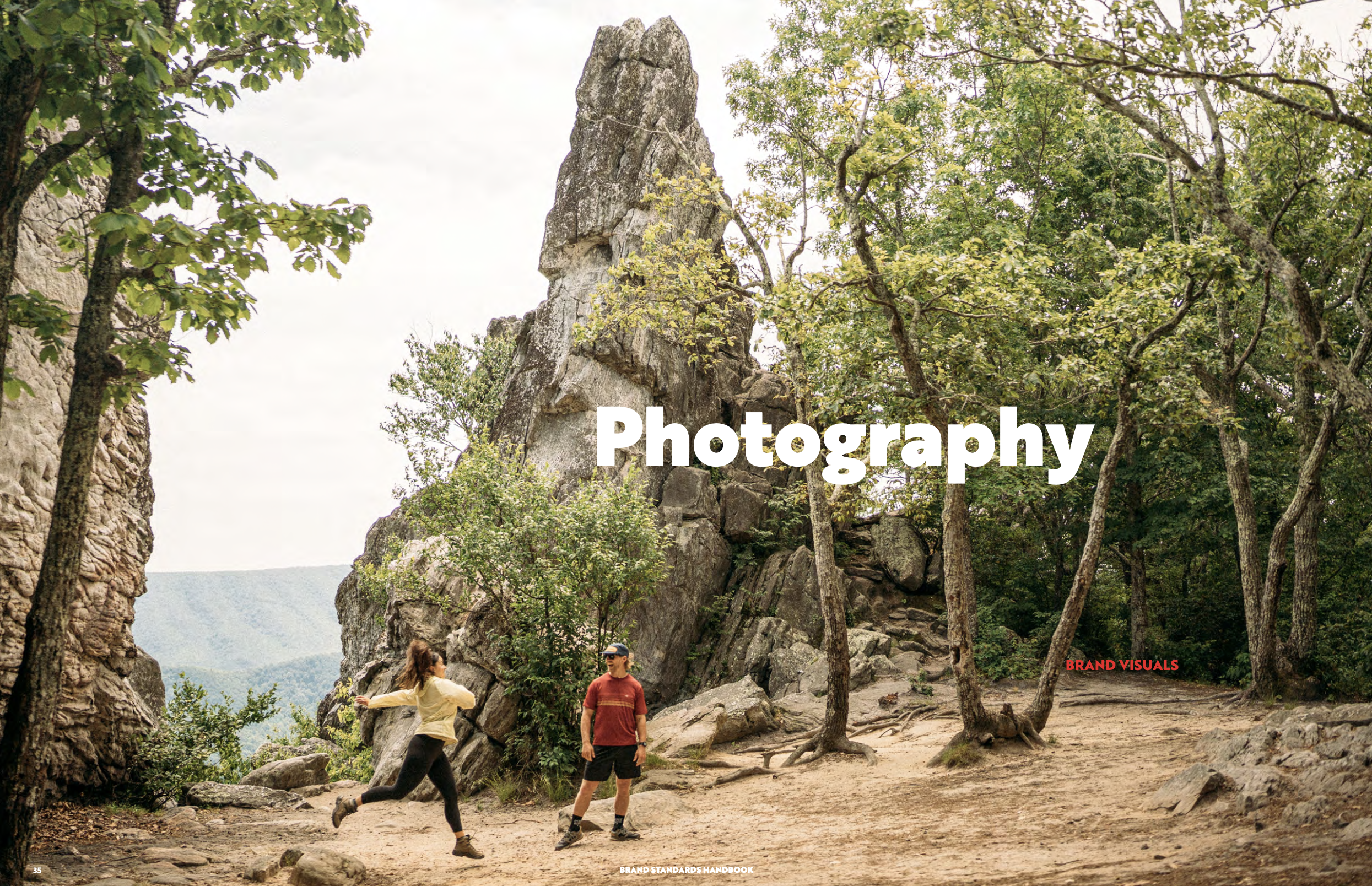 Two women and a man are on a rocky trail in a forested mountain area, with large trees and a tall rock formation in the background. One woman is running or jumping, and the other two people are standing and facing each other. Bright daylight filters through the trees. The word 'Photography' is overlaid on the image.