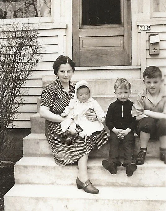 Miriam Howden holding Mary next to Tom and Mike on steps outside of their home.