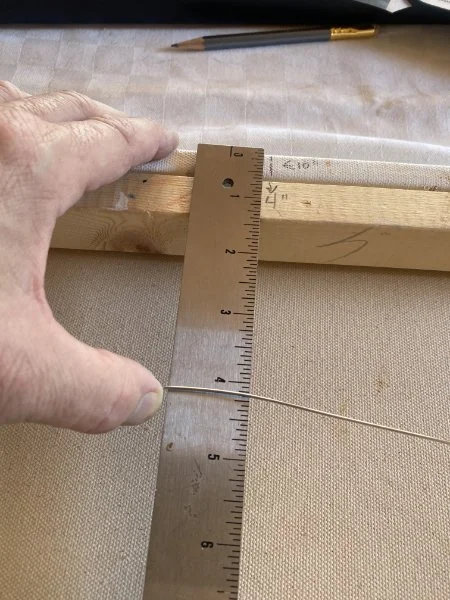 a man's hand holding a ruler and the hanging wire of a painting, measuring the distance from the top of the frame