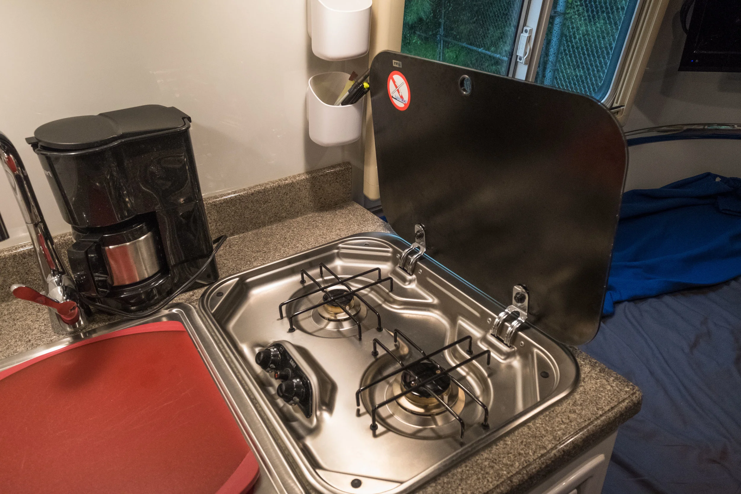 The stove uncovered, sink with a cutting board we found that nestles inside the sink to provide extra counter space. On the wall we have two magnetic pods that are great for phone, pencils, salt and pepper, lots of stuff and they stay put.