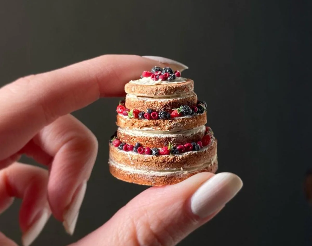 A tiny berry-topped cake held between two fingers