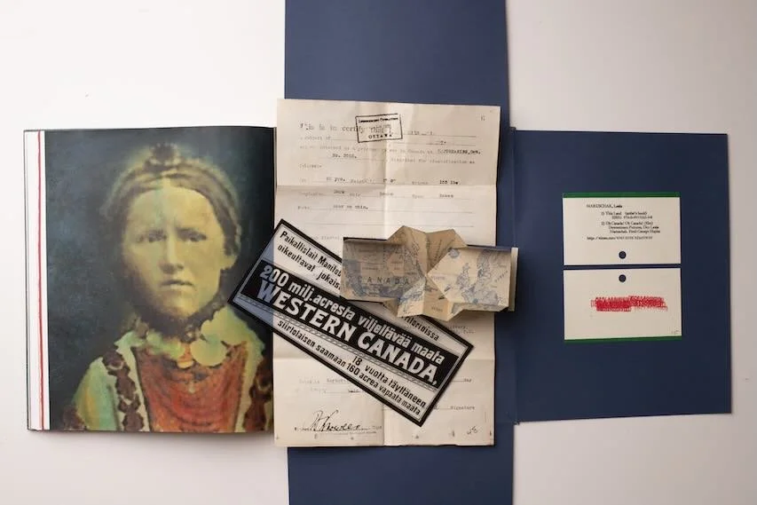 Collection of documents including a photograph of a young girl with braided hair, an old handwritten document, a folded map, a sticker indicating land in Western Canada, and a blue booklet.
