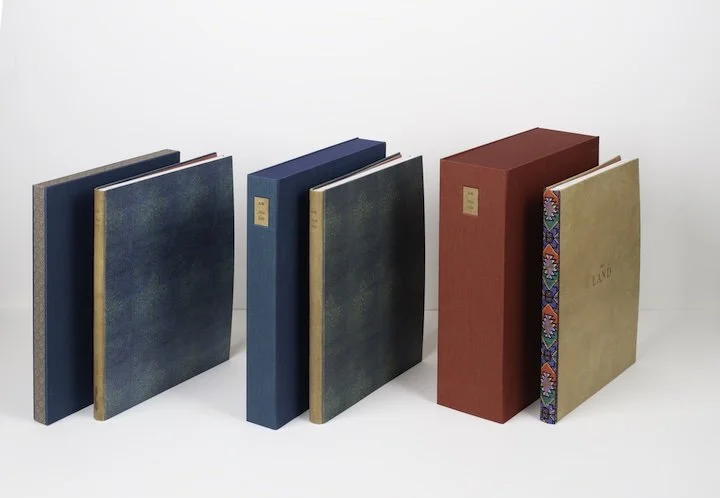 A collection of four hardcover books with decorative spines, standing upright on a white surface against a white background.