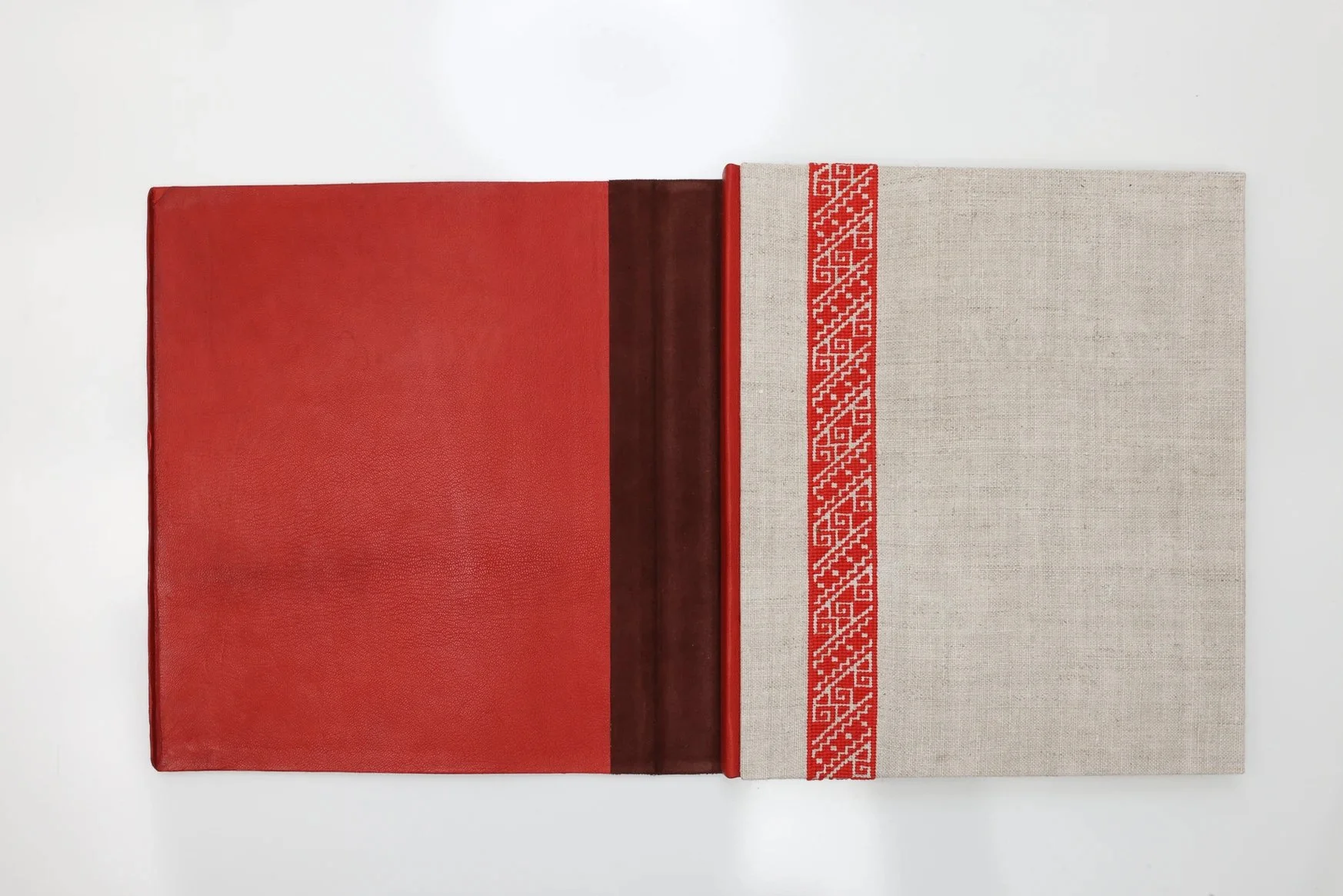 Open book with red cover and beige linen cover decorated with a red geometric border design.