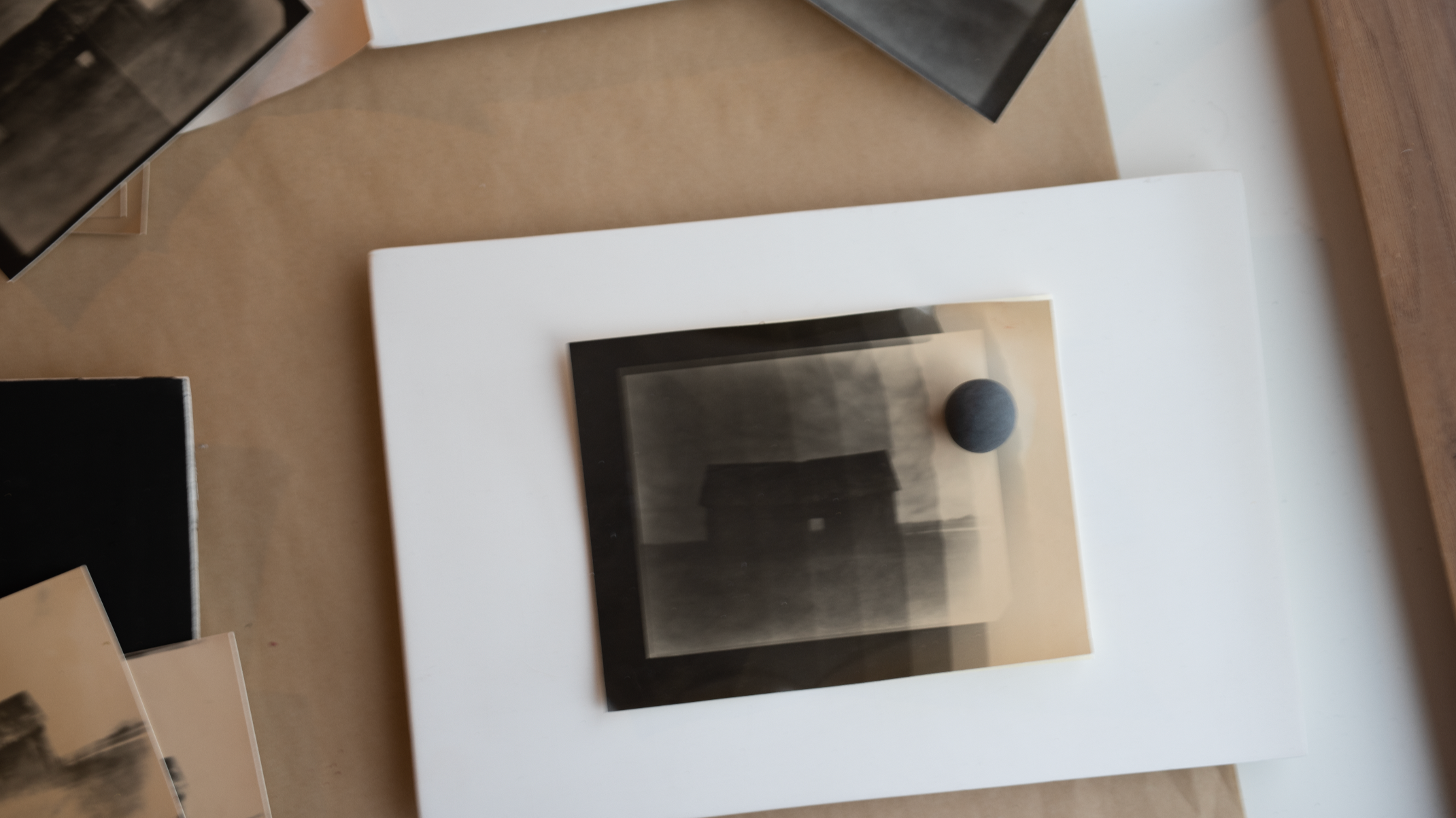 A framed black and white photograph with a small black stone on top, displayed on a white pedestal in an art gallery.