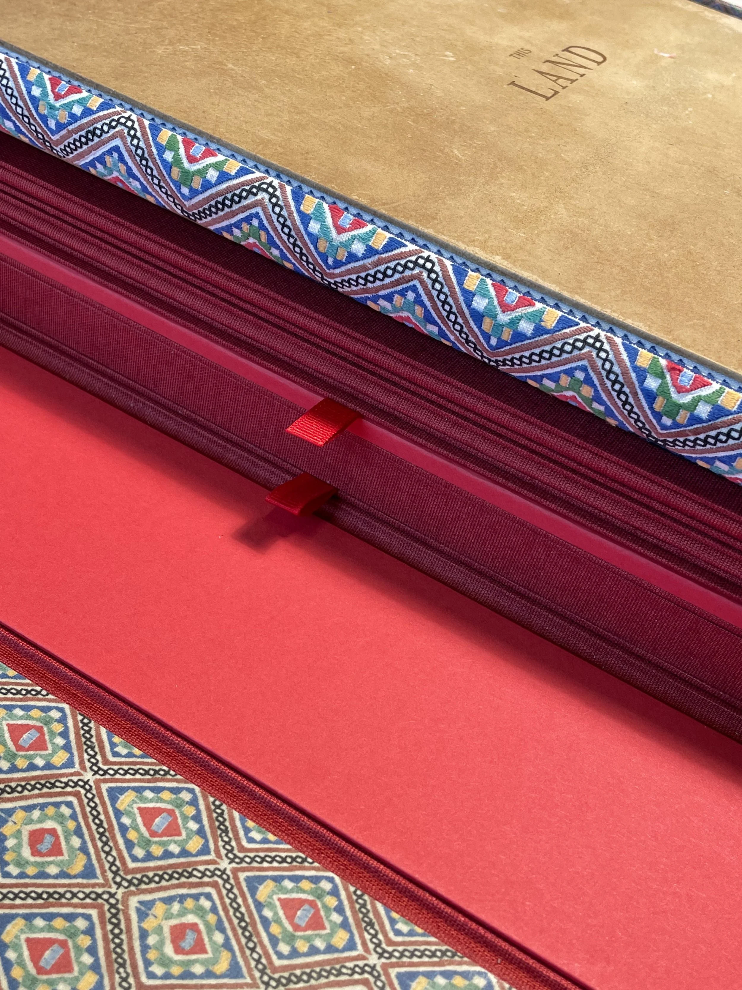 Close-up of a colorful patterned sewing box with a textured brown lid and red storage compartments, resting on a decorative tiled surface.