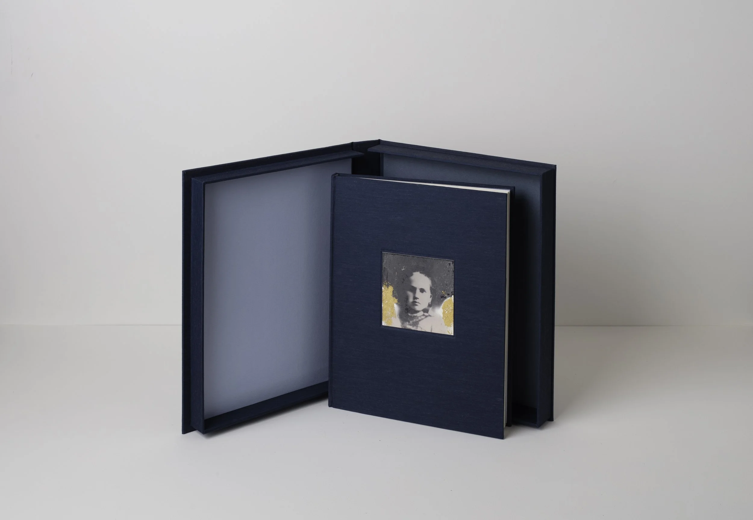 A navy blue photo album with a black-and-white portrait on the cover, open to reveal empty pages, placed against a light-colored background.