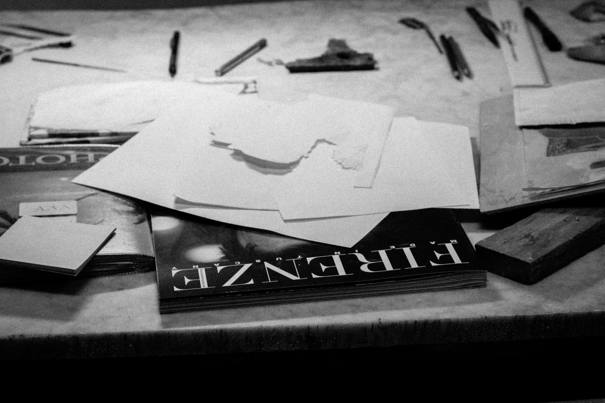 A cluttered tabletop with scattered papers, a magazine, and various writing and drawing tools.