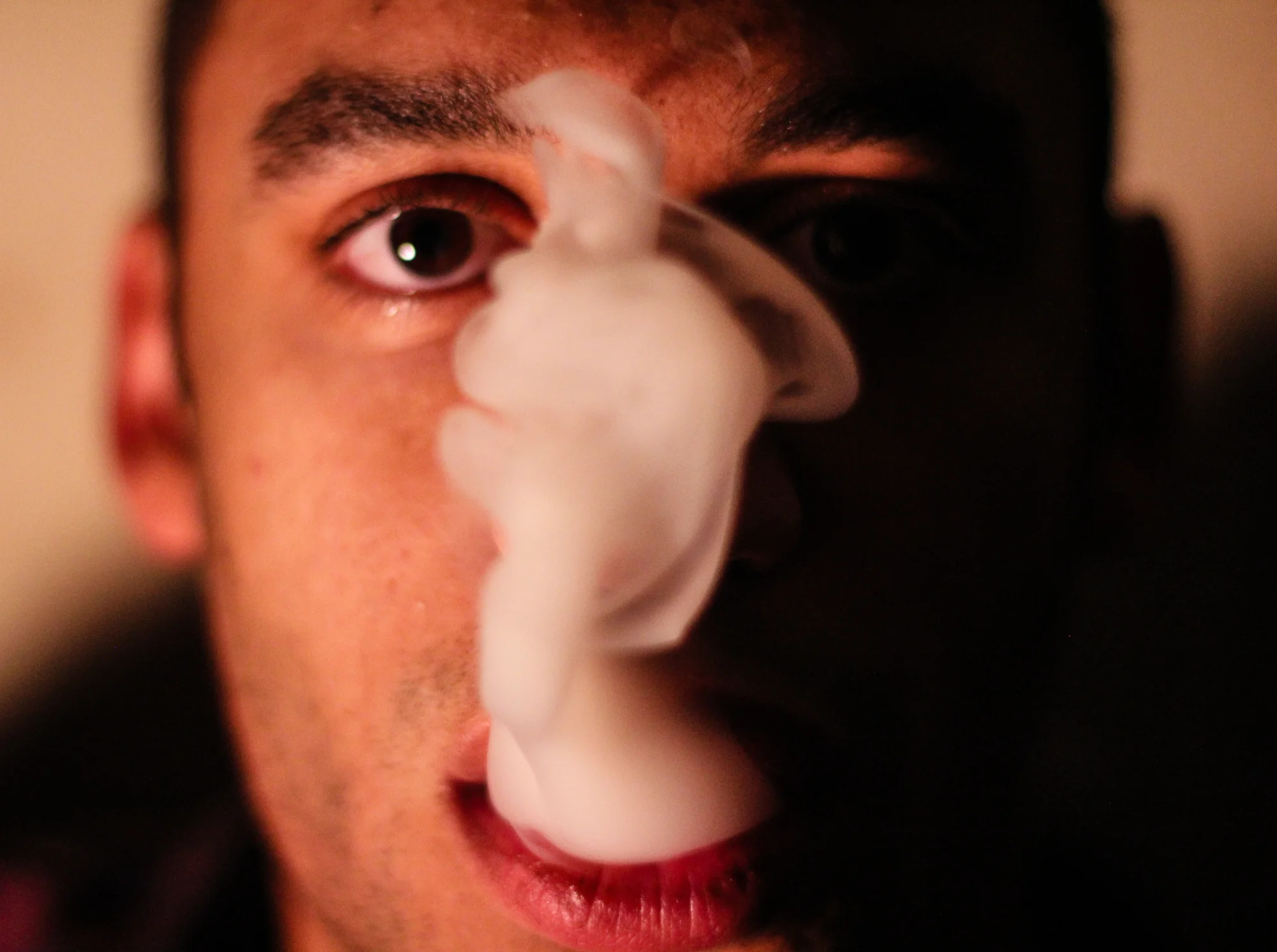 Close-up of a person's face with smoke covering the nose, some of the smoke obscures half of the face, with brown eyes and dark eyebrows.
