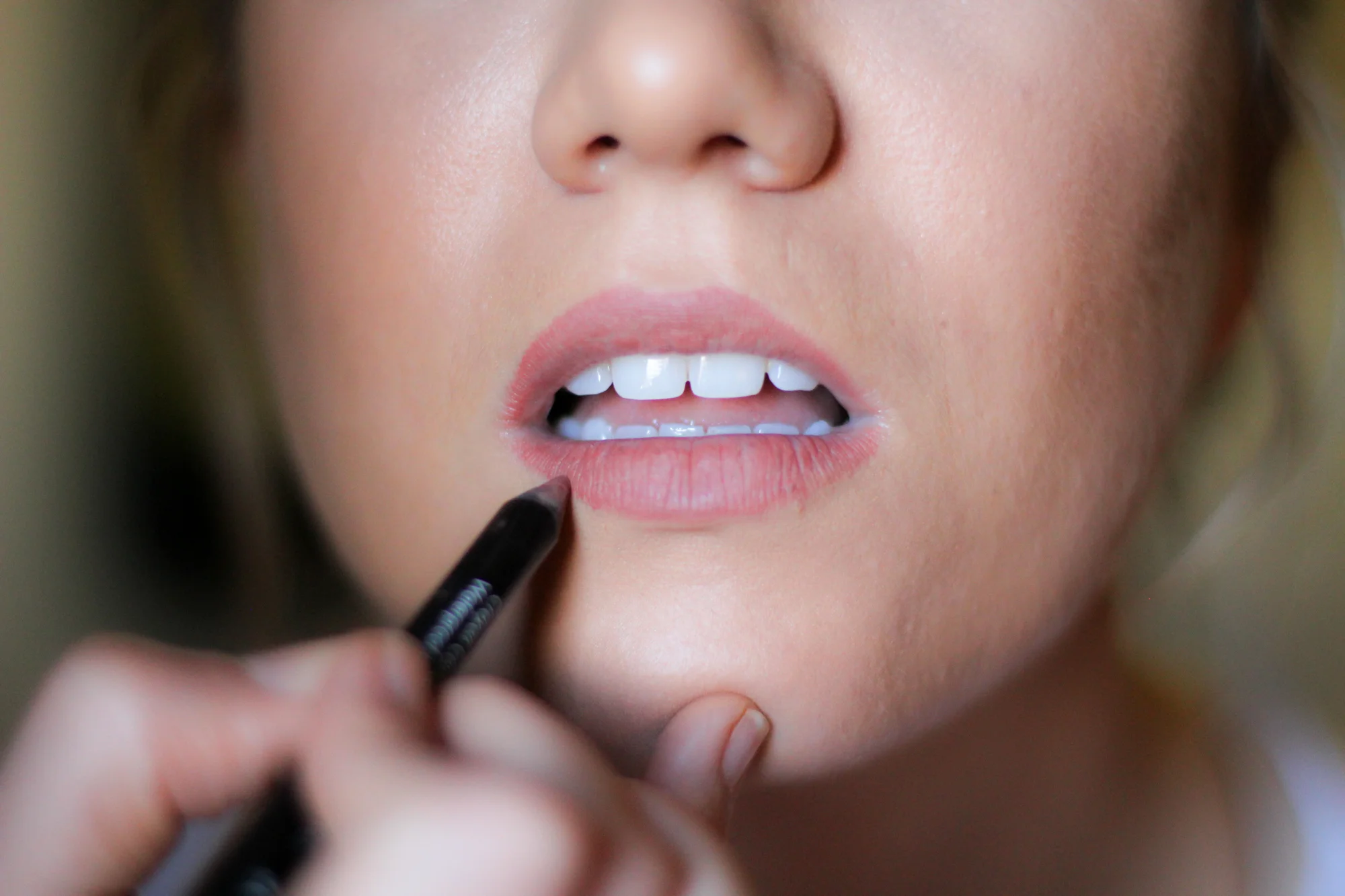 Close-up of a woman applying lipstick to her lips with a black lip liner