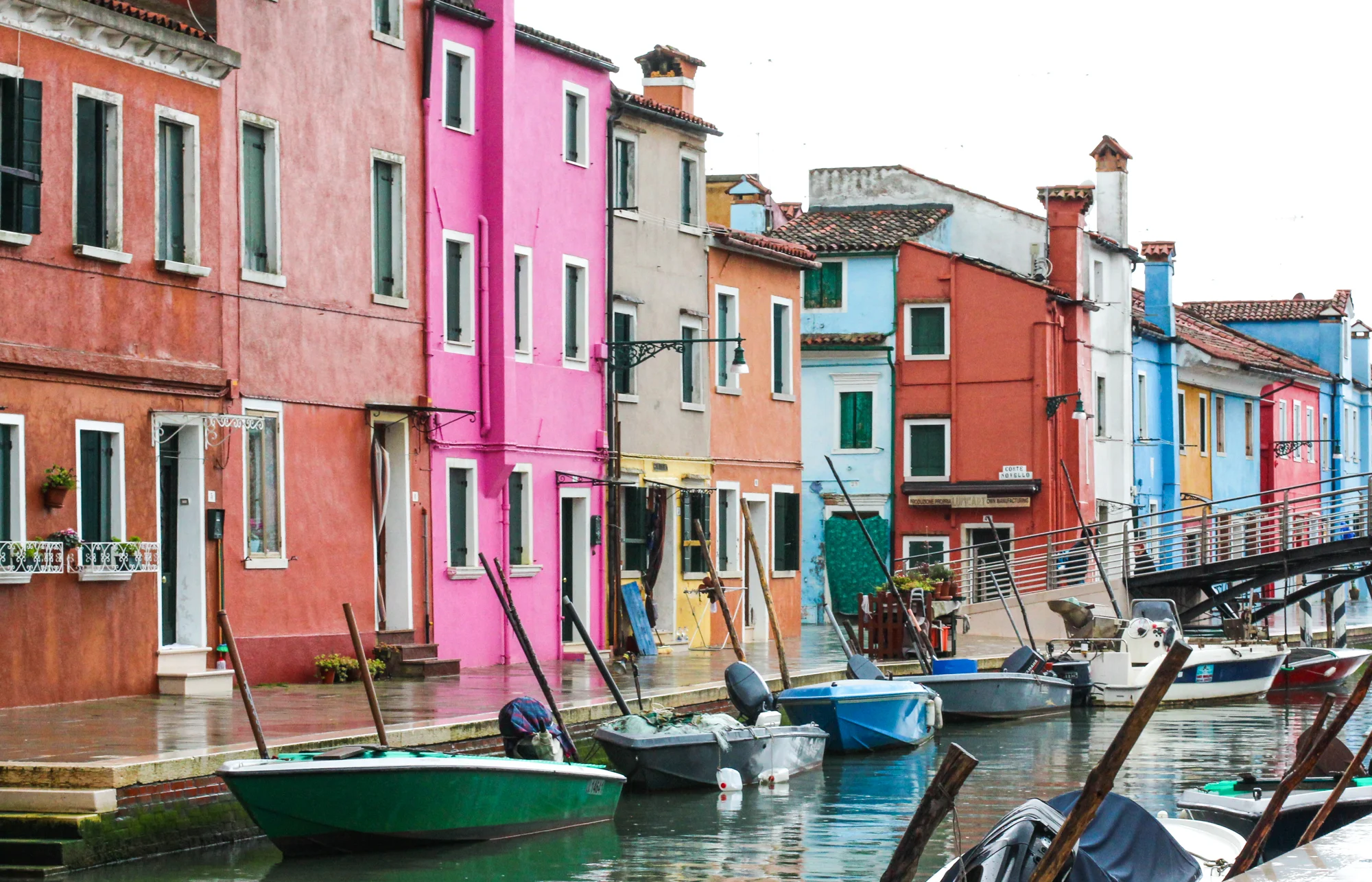 Colorful buildings along a canal with boats docked in front, with some buildings in pink, blue, yellow, and orange.