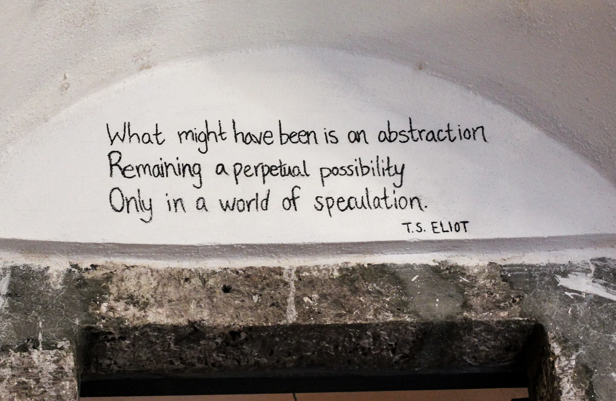 A quote by T.S. Eliot written on a wall above a stone fireplace mantle that reads: "What might have been is an abstraction Remaining a perpetual possibility Only in a world of speculation."