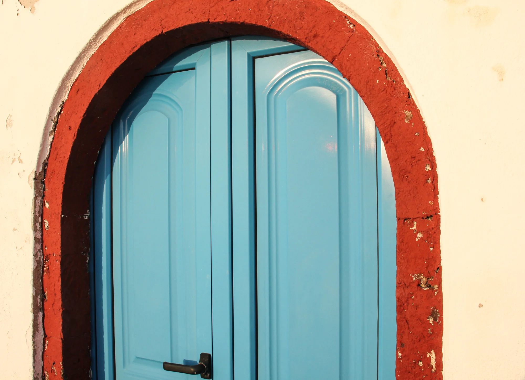 Blue arched door with black handle set in a wall with red brick trim and white plaster.