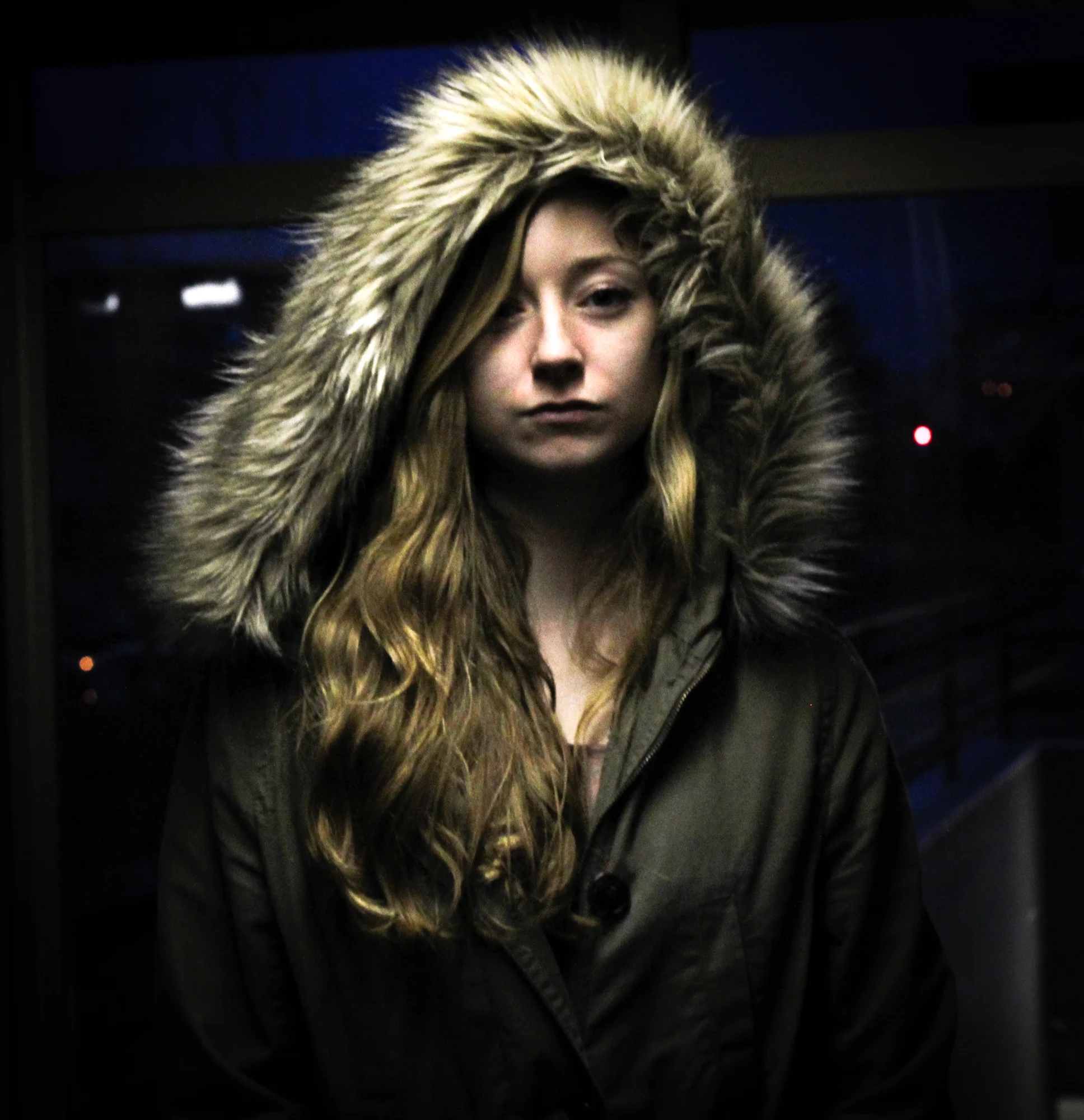 A young woman with long wavy hair wearing a dark winter coat with a large fur-lined hood.