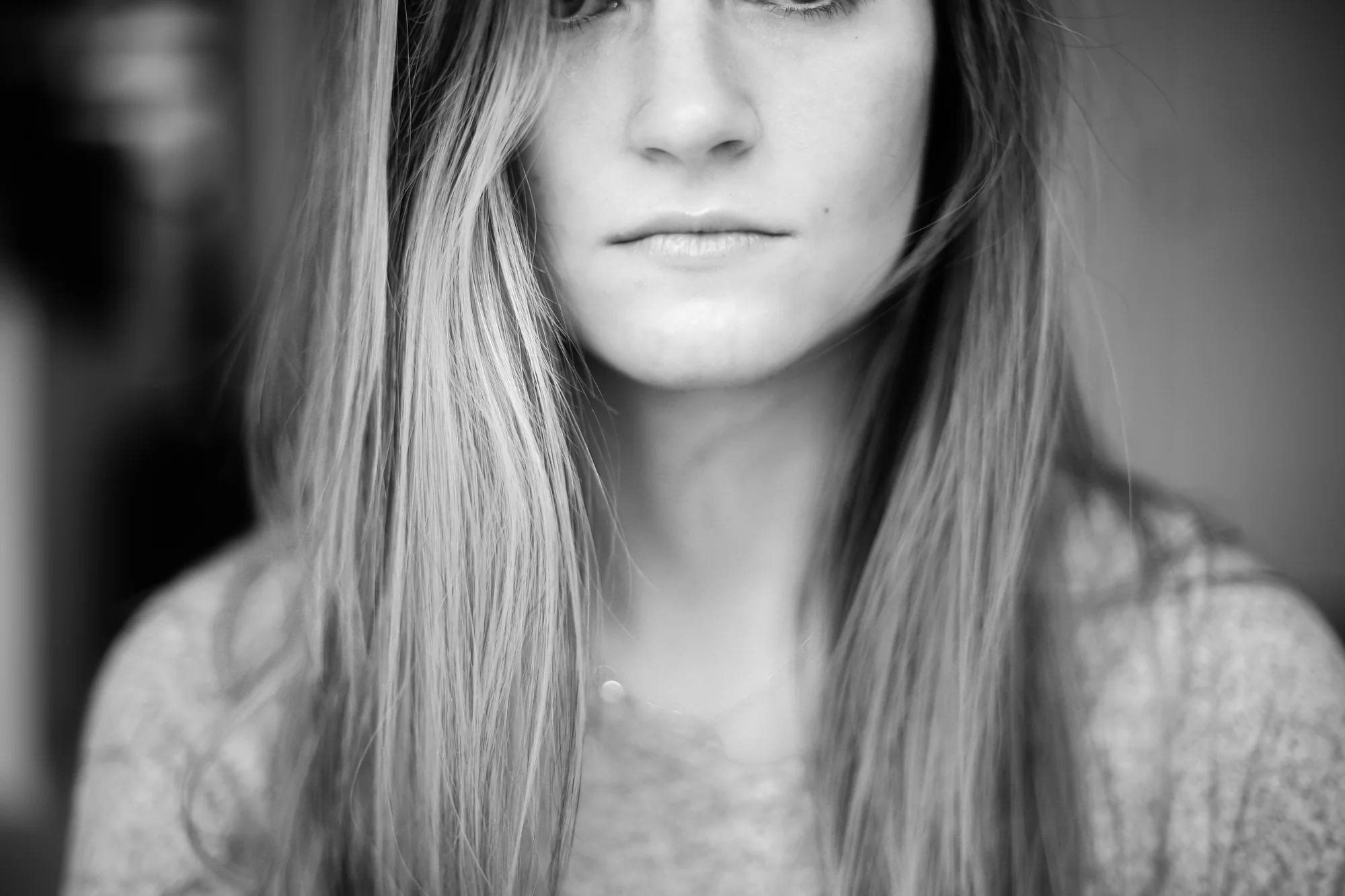 Black and white close-up photo of a woman with long, straight hair, partially covering her face, with a neutral expression.