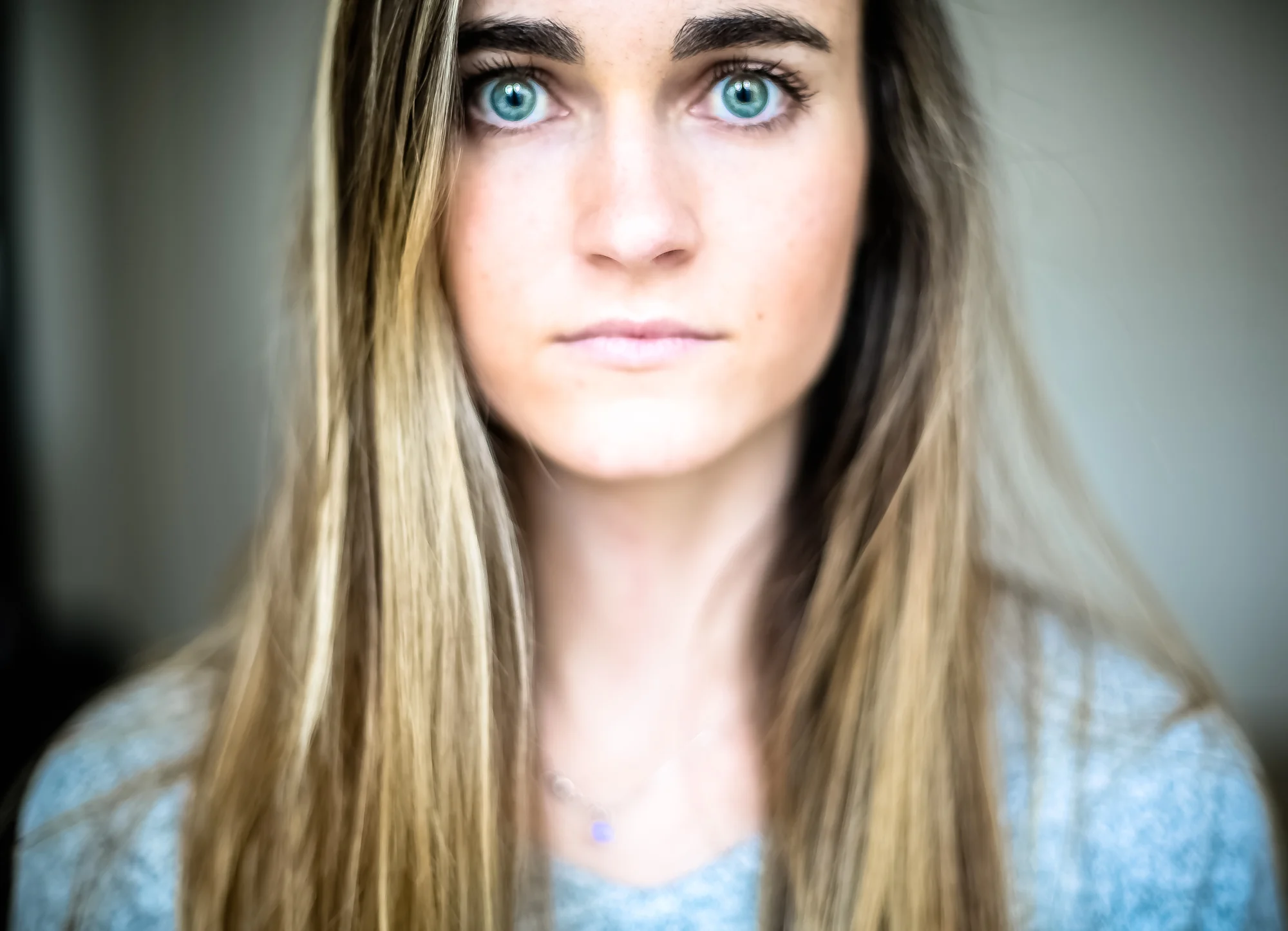 Close-up of a young woman with long, light brown hair and striking blue eyes, looking directly at the camera.