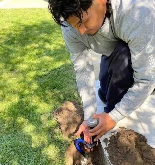 An irrigation specialist working on a sprinkler head in Redwood City, CA.
