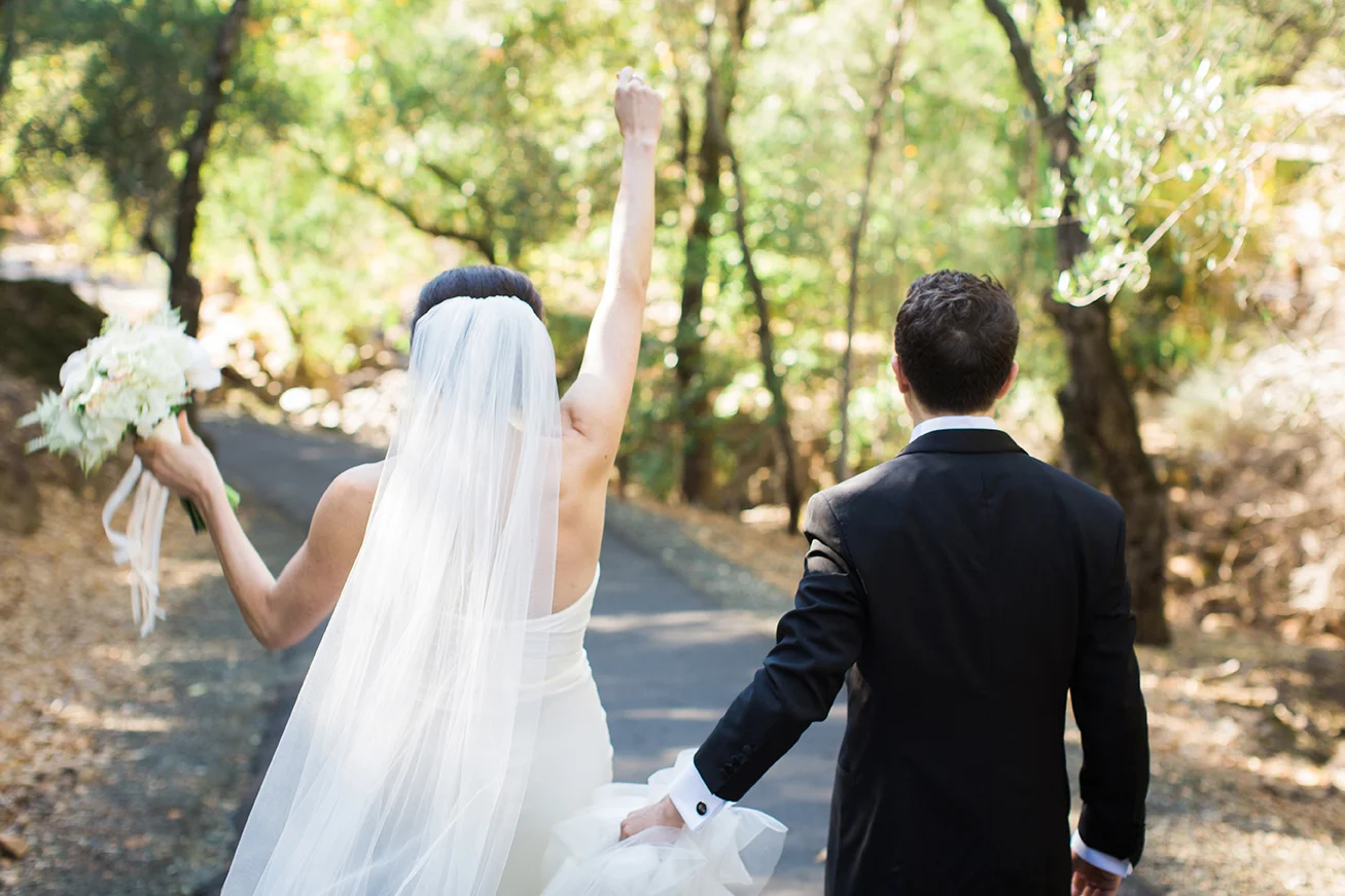 Bride punches her fist in the air in celebration while groom holds her dress at Auberge du Soleil.