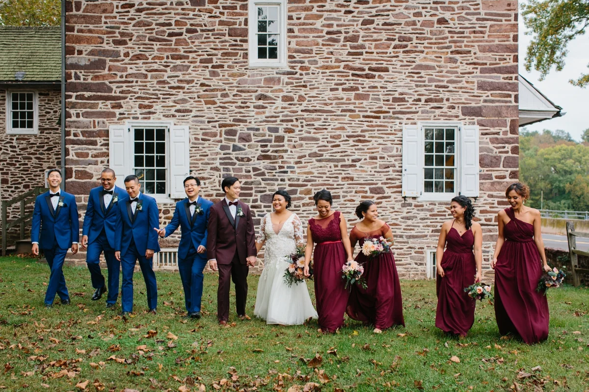 The wedding party takes a stroll in front of the historic stone buildings that sit along the Delaware river at Washington Crossing Park.