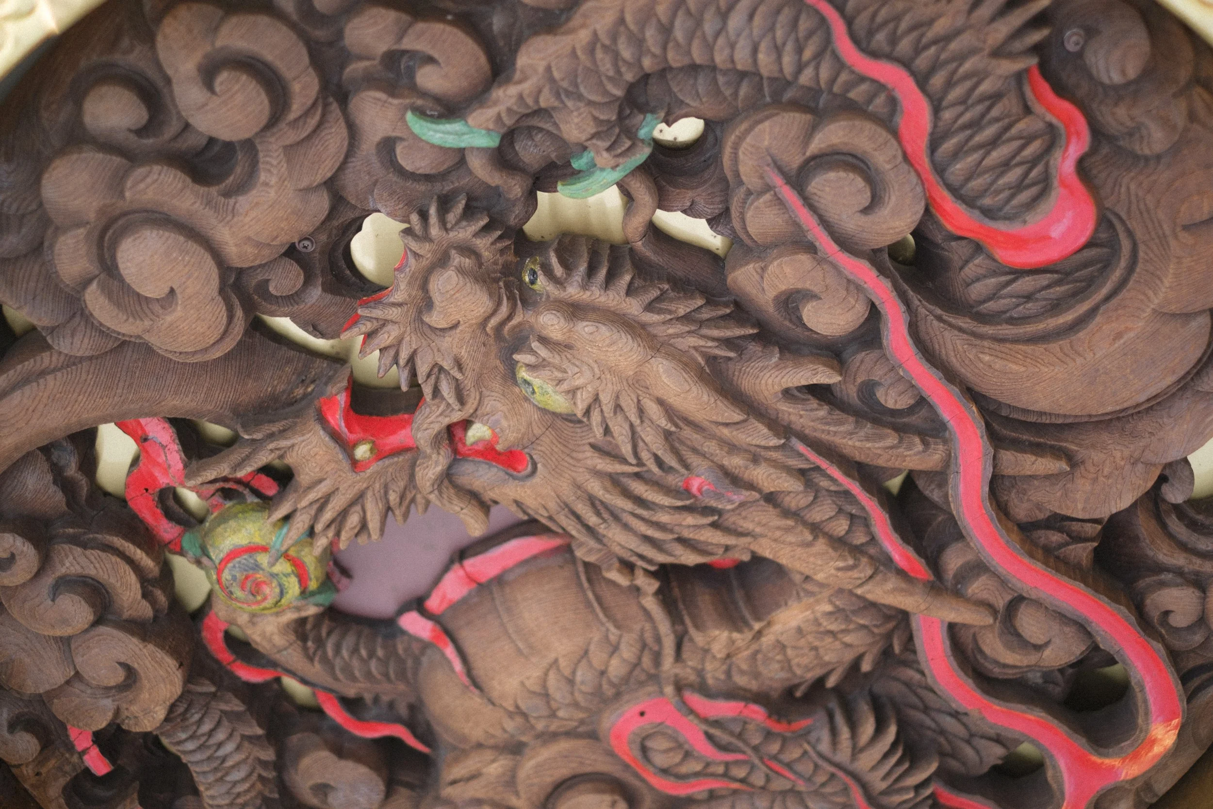 A detailed wooden carving of a dragon intertwined with swirling clouds, painted in brown with red and green accents.