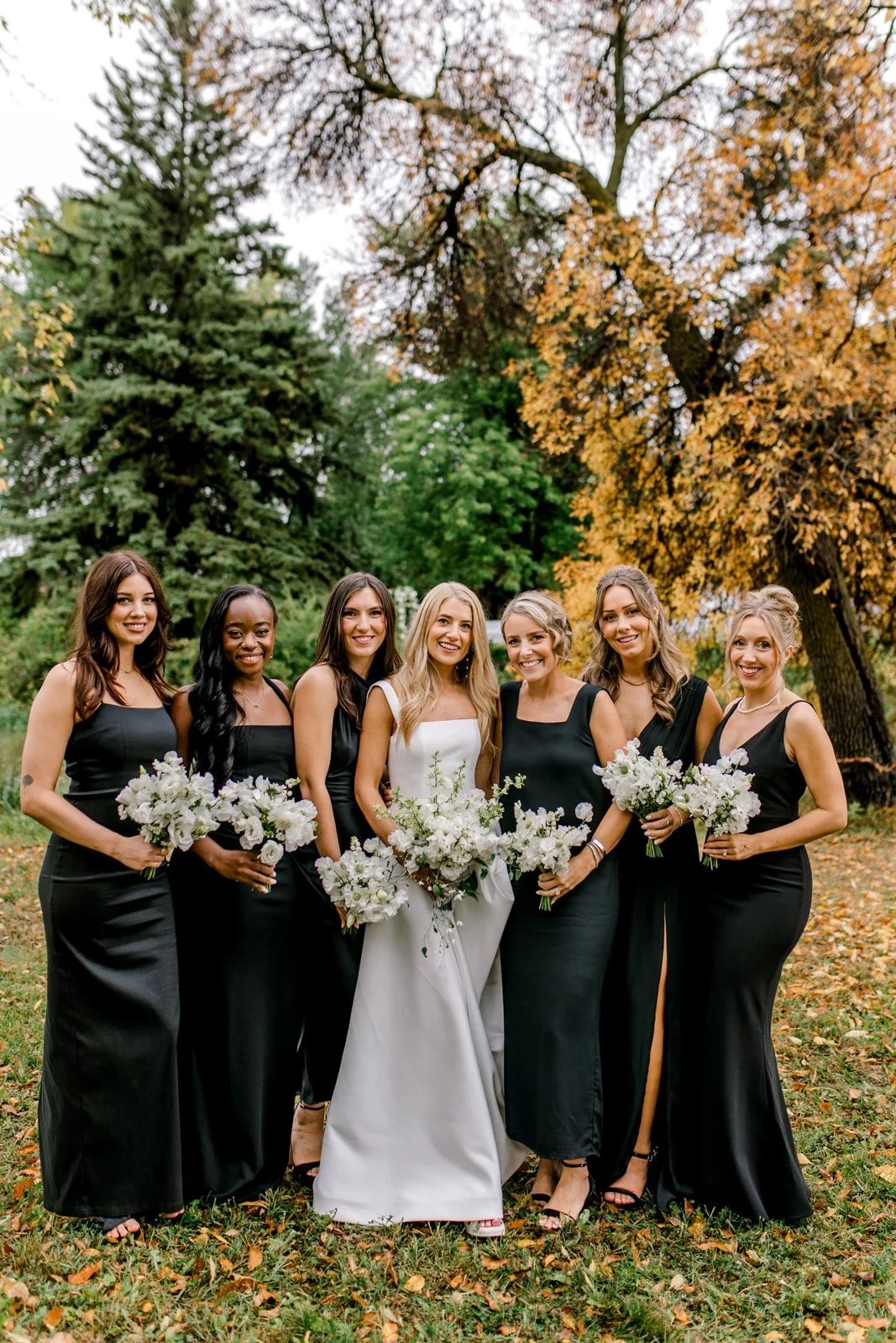 Bridesmaids in Long Black Dresses surrounding Bride in White Gown with White Bouquets