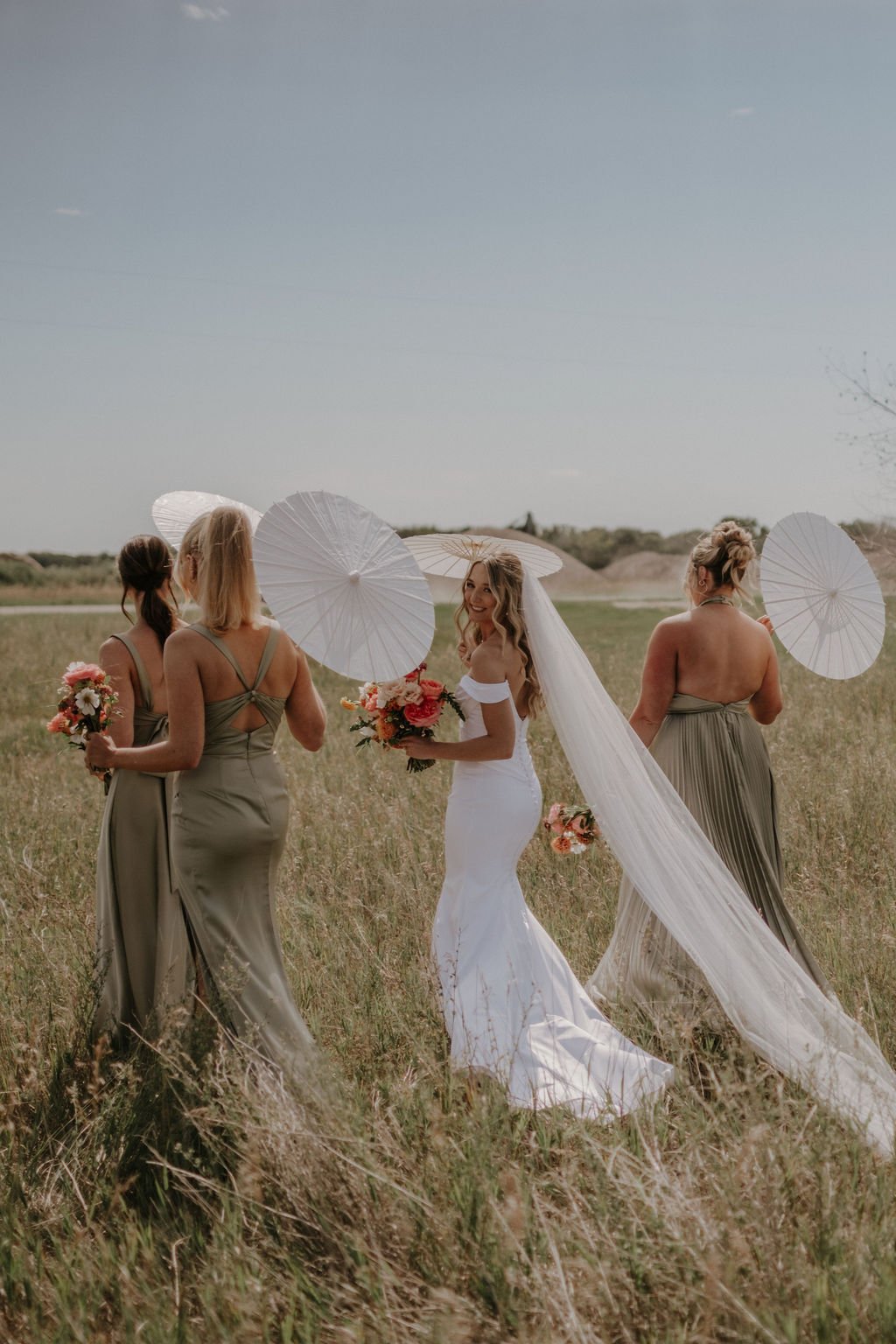 Bridesmaids and Bride Walking Through a Field Holding White Parasols