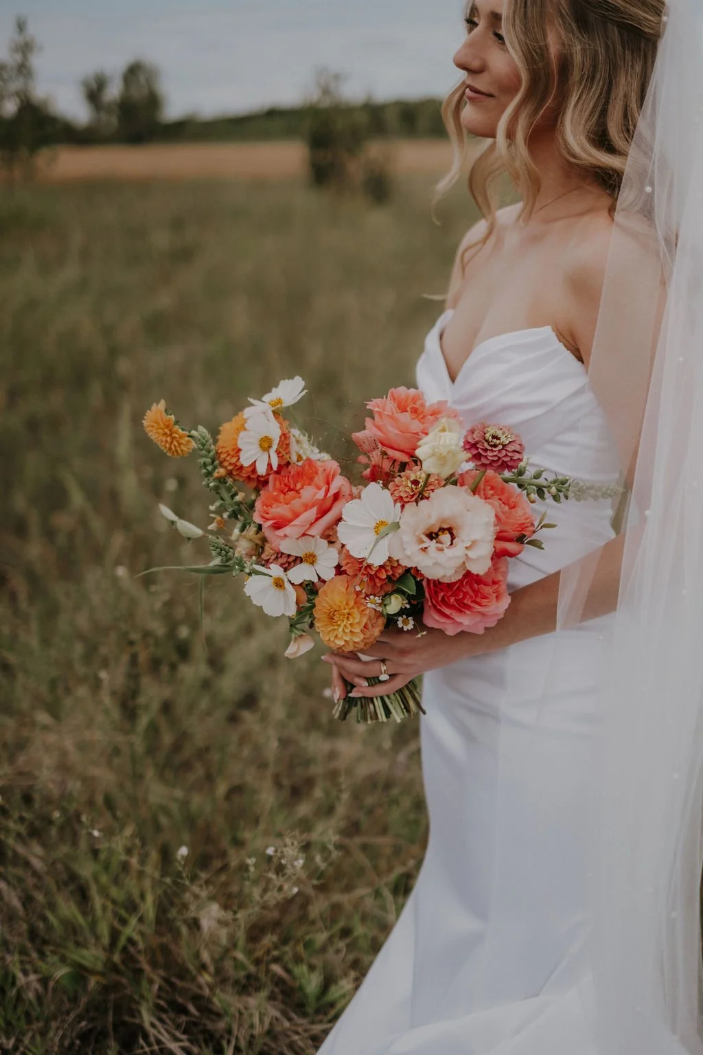 Caucasian Bride holding Wedding Bouquet with Coral Roses and Peach Lisianthus Flowers