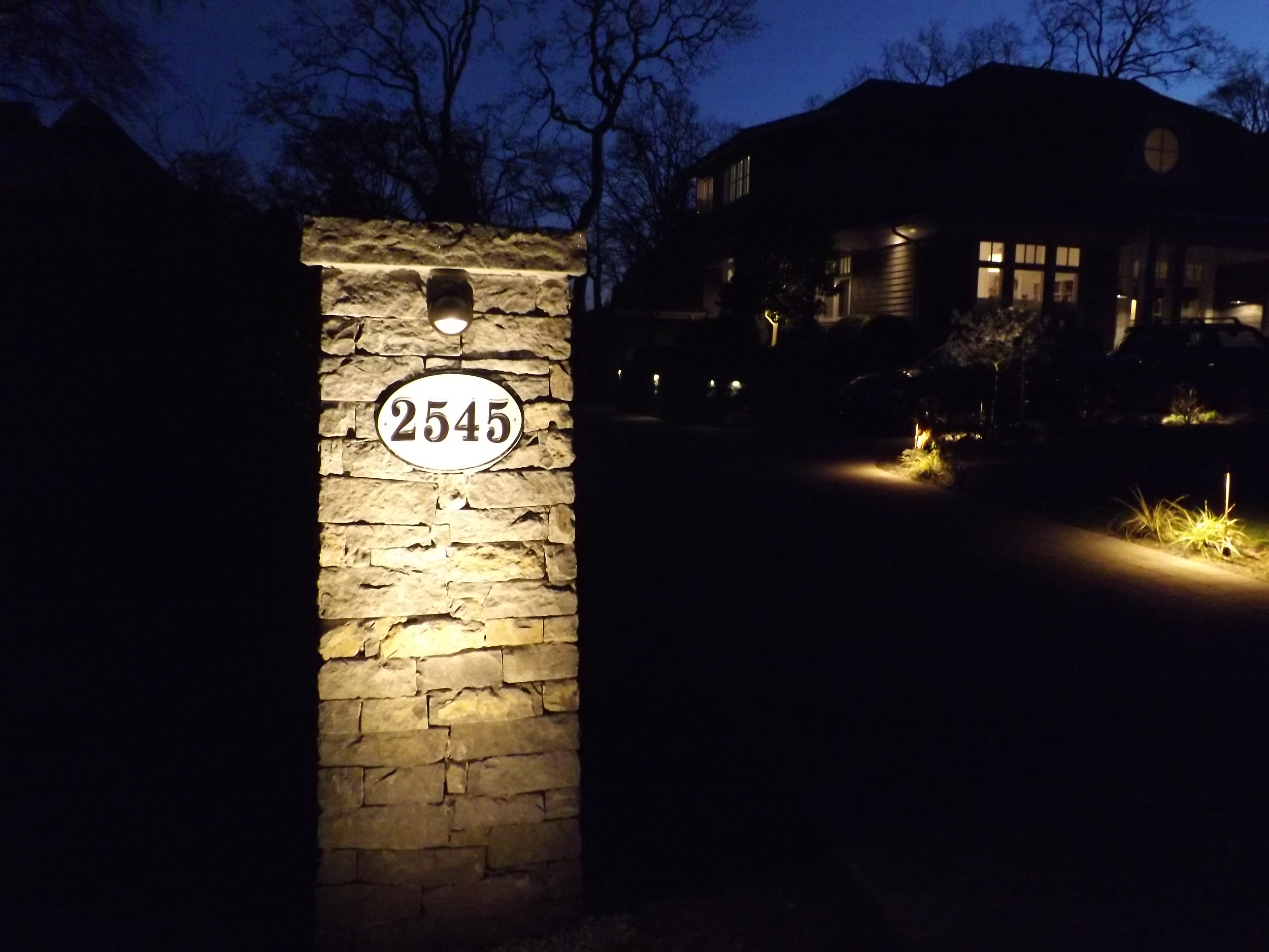 tHE LIGHTING PLAN FOR THIS LANDSCAPE INCLUDES ILLUMINATING THE bASALT ENTRANCE PILLAR AND STREET NUMBER, CASTING A WARM GLOW ALONG THE DRIVEWAY.