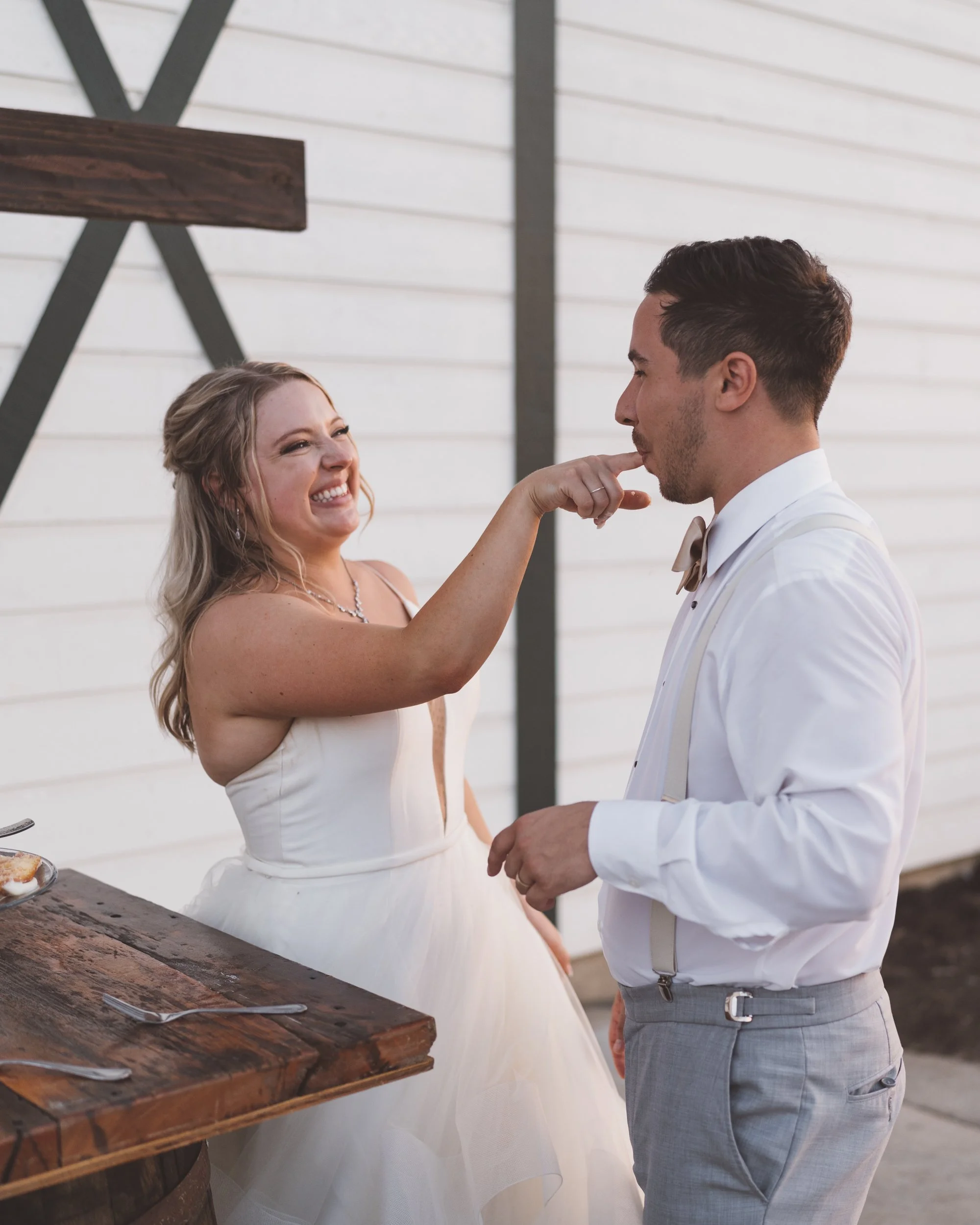 A woman in a wedding dress playfully touching a man's lips at an outdoor wedding reception.