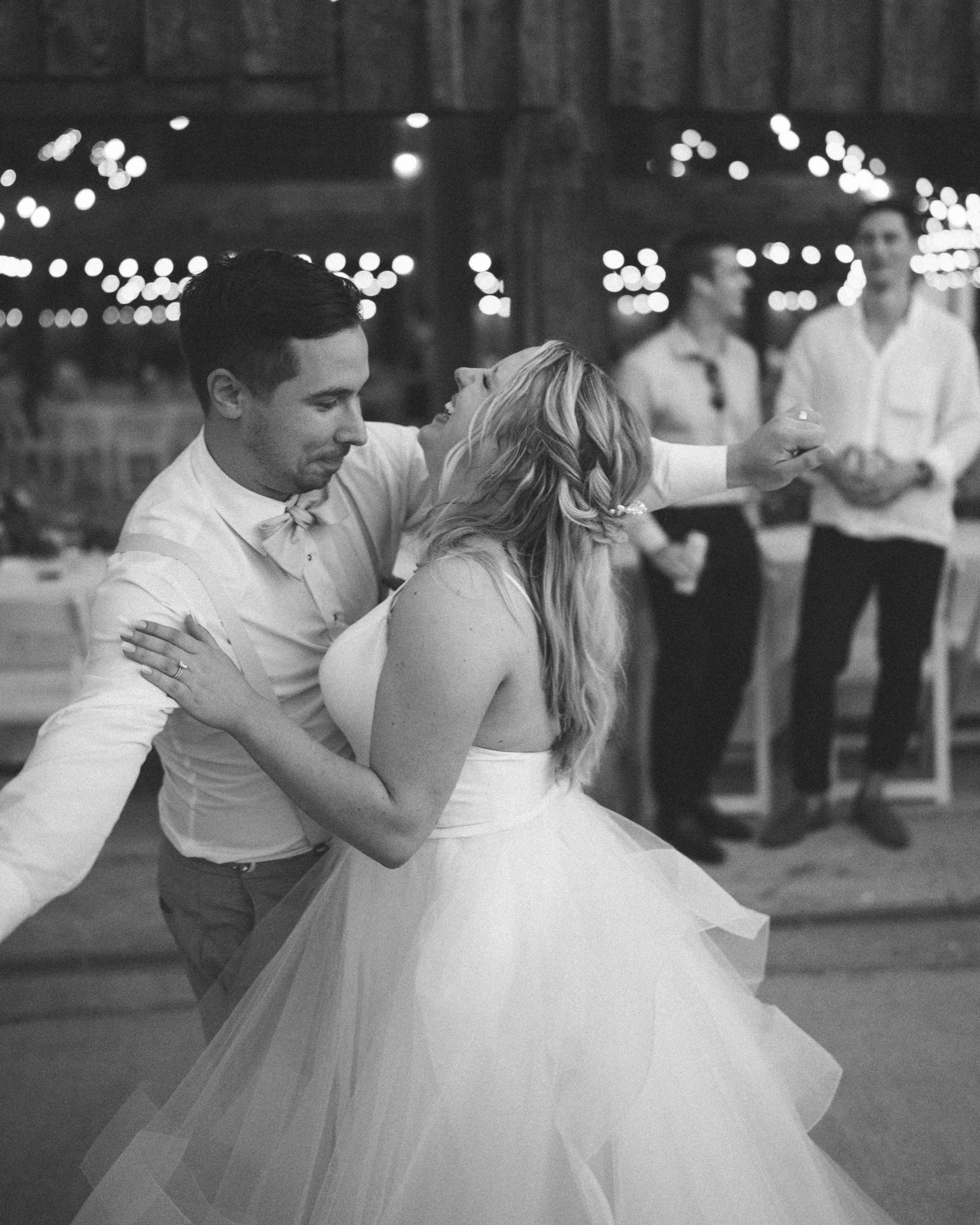 Black and white photo of a wedding reception dance, with a couple dancing closely in the foreground, and other guests in the background.
